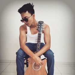 Young man playing guitar against wall