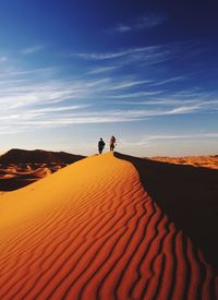 People on sand dune in desert against sky