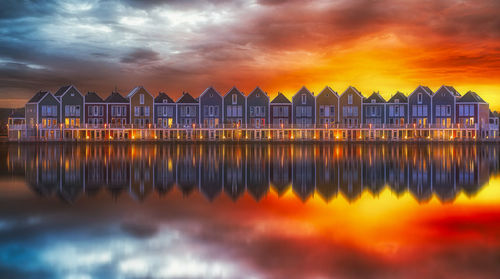 Reflection of buildings on sea against cloudy sky during sunset