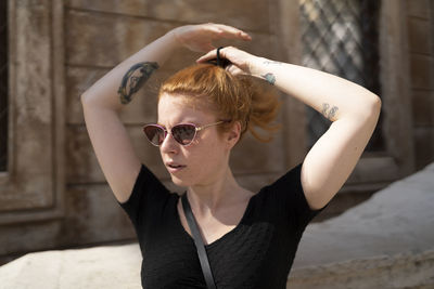 Ginger woman with sunglasses is straightens her hair alone in sunlight