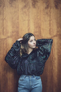  young woman looking away standing against wooden wall