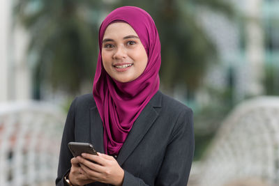 Portrait of a smiling young woman using smart phone outdoors