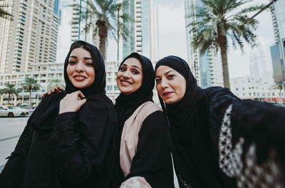 Portrait of cheerful women standing against buildings in city