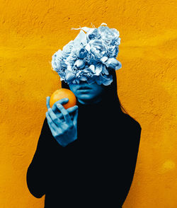 Close-up of hand holding flower against yellow wall