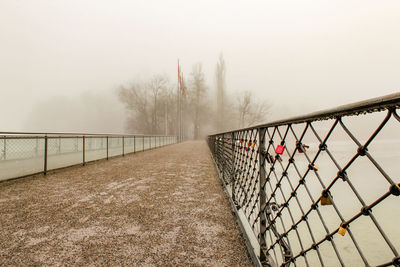 Footbridge by fence against sky during winter