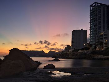 Sea by rocks against sky during sunset