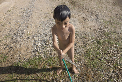 Naked boy playing with water pipe at yard