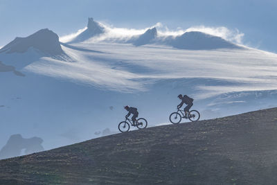 Men riding bicycle on mountain against sky