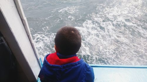 Rear view of girl looking at sea seen through window