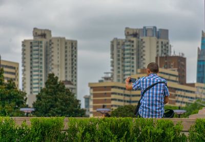 Rear view of man standing by cityscape against sky