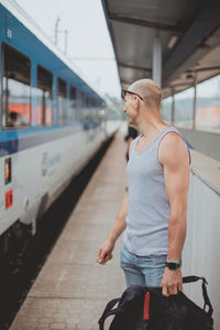 Young man in a t-shirt on the platform waiting for a train using mobile phone. man by train 