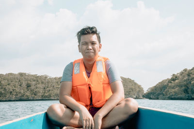 Young man sitting in boat against sky