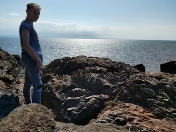 Man standing on rock by sea against sky