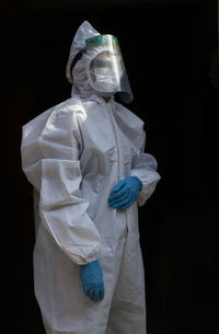 Portrait of woman wearing protective suit standing against black background