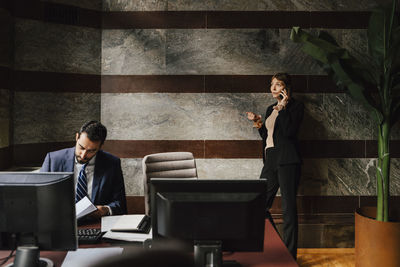 Businesswoman talking on smart phone while male colleague working at law office