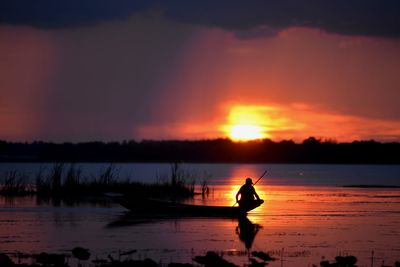 Silhouette man in lake against sky during sunset