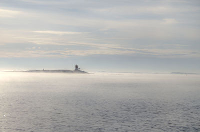 Lighthouse by sea against sky on sunny day