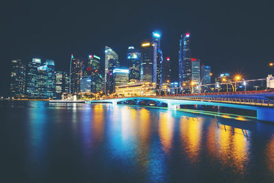 Illuminated buildings by river against sky at night