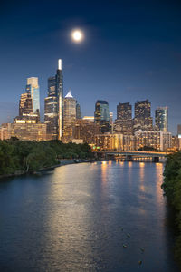 Illuminated buildings by river against sky in city