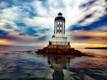 Lighthouse by sea against sky during sunset