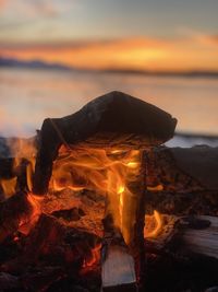Bonfire on wooden log against sky during sunset