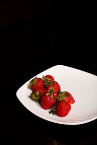 Close-up of strawberries in plate against black background
