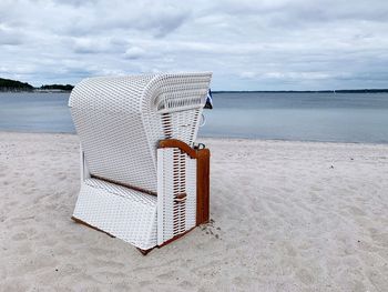 Hooded chairs on sand at beach against sky