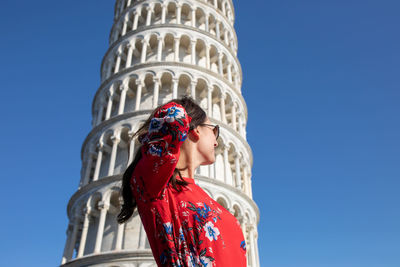 Woman with hand in hair standing against leaning tower of pisa in italy