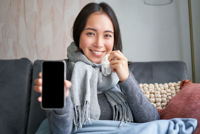 Portrait of young woman using mobile phone while sitting on bed at home