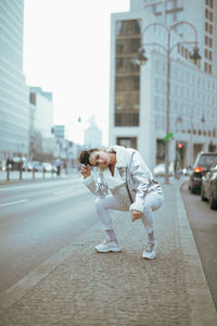 Portrait of woman crouching on footpath in city