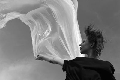 Low angel view of woman holding textile against sky