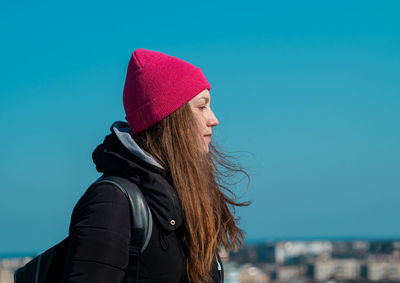 Young woman long hair in pink hat black coat blue sky background. stylish millennial girl walking