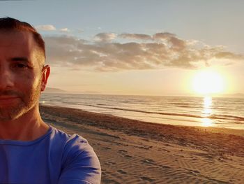 Portrait of young man on beach against sky during sunset