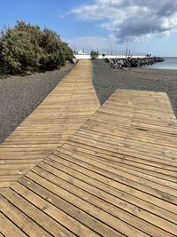 Surface level of boardwalk on beach against sky