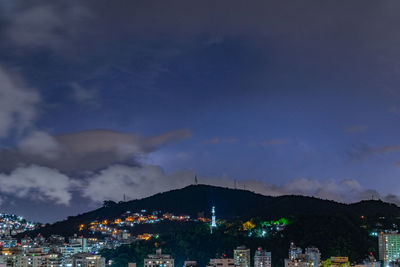 Illuminated buildings in city against cloudy sky