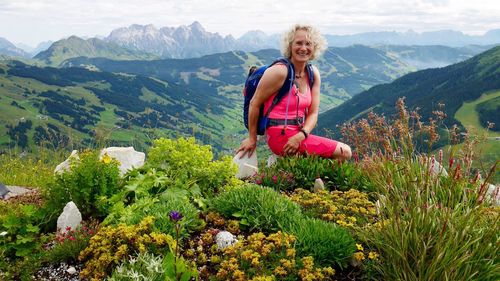 Portrait of smiling woman sitting amidst flowers growing on field against zwolferkogel mountain
