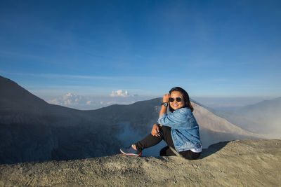 Portrait of young woman sitting on mountain against sky