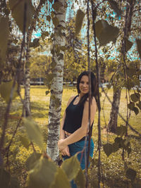 Portrait of young woman standing by tree in forest
