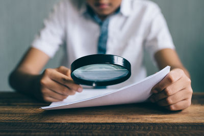 Midsection of boy holding paper and magnifying glass at table