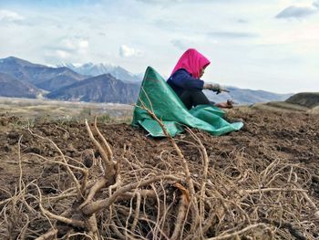 Man sitting on mountain against sky