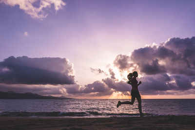 Rear view of man standing at beach against sky during sunset