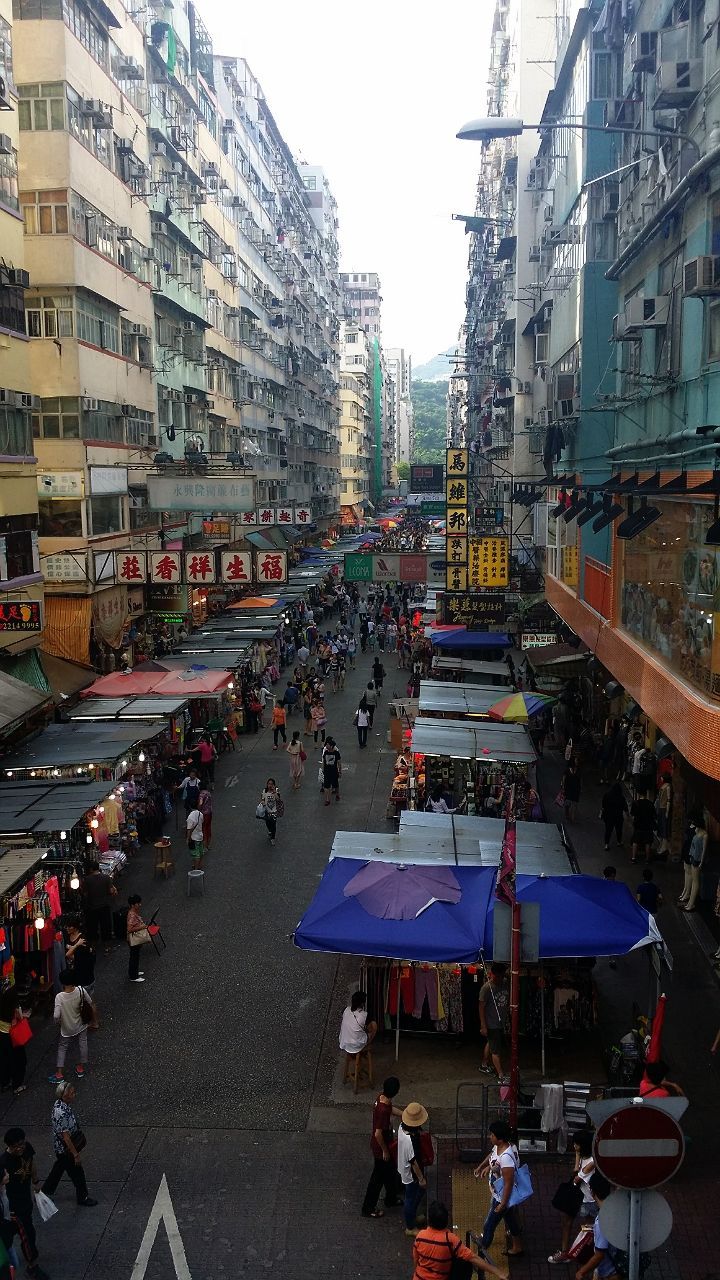 large group of people, building exterior, architecture, street, person, city, built structure, men, city life, lifestyles, crowd, leisure activity, mixed age range, city street, high angle view, walking, transportation, road, outdoors