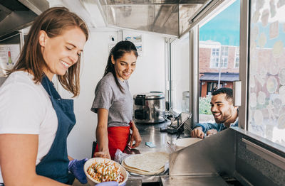 Happy young female owners preparing fresh tex-mex while talking with male customer