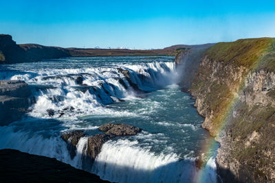 Iceland's famous gullfoss waterfall powerfully surging down with a rainbow in front.