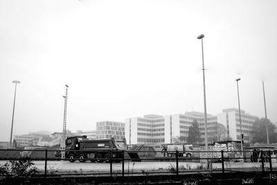 Trucks on street by buildings in city against clear sky