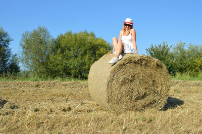 Low angle view of smiling young woman sitting hay bale