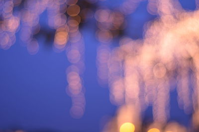 Defocused image of illuminated lights against sky at night