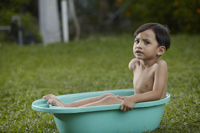 Portrait of shirtless boy sitting in bathtub on field at yard