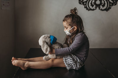 Girl holding toy while sitting on floor at home