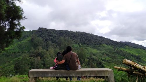 Rear view of men sitting on mountain against sky